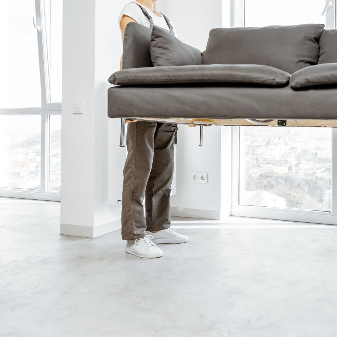 Men picking up a sofa and moving it across a concrete floor.