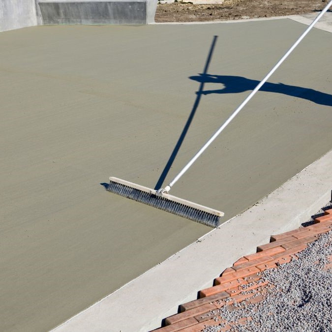 A broom being dragged along wet concrete to give it a brushed effect.