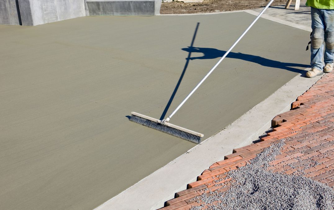 A broom being dragged along wet concrete to give it a brushed effect.